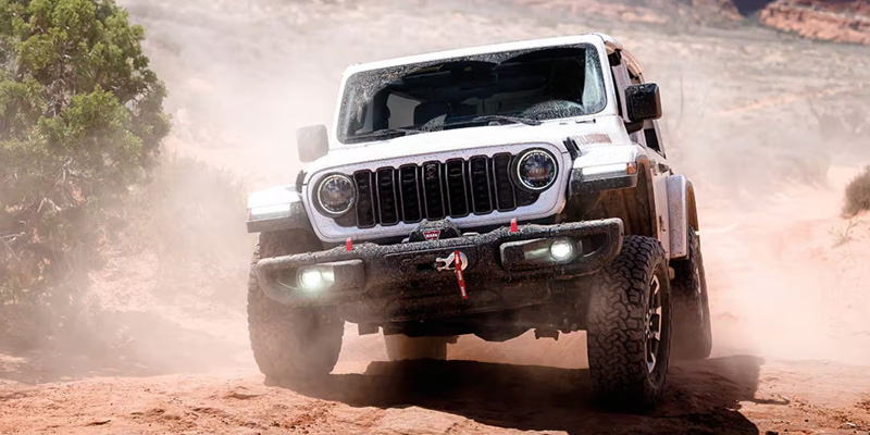 A white Jeep Wrangler navigating through a vast desert landscape.