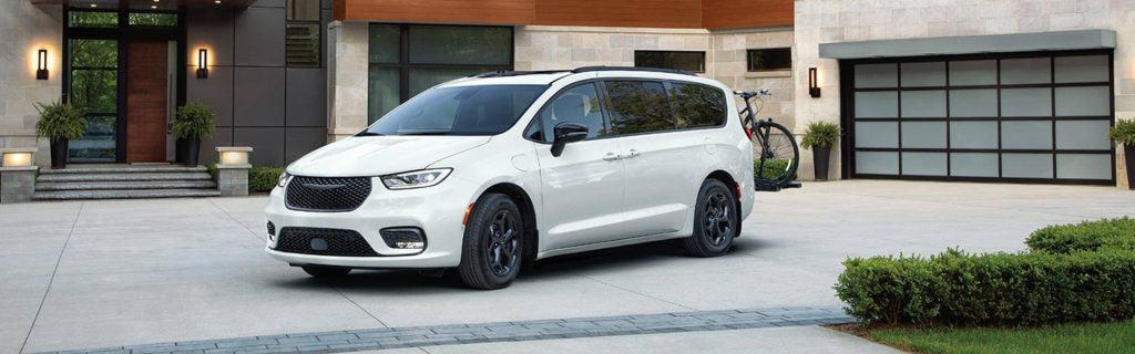 A white Chrysler Pacifica parked in a driveway in front of a contemporary house with a bike mounted on the back.