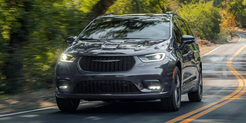 A gray Chrysler Pacifica minivan driving on a winding road surrounded by trees.