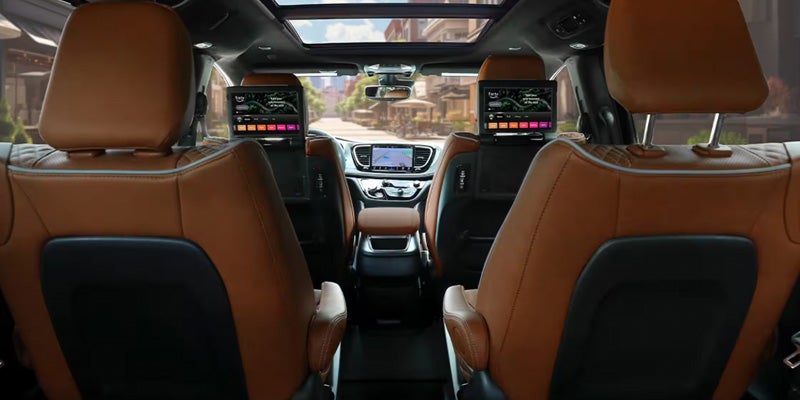 Interior view of a Chrysler Pacifica with brown leather seats, showing the back seat area and dashboard screens.