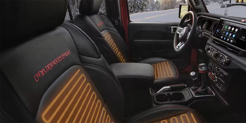 Interior shot of a Jeep Wrangler showcasing the front seats, featuring black leather with orange striped accents and detailed stitching.