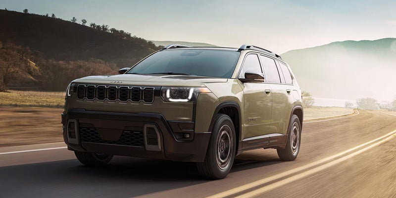 A Jeep Cherokee SUV driving on a scenic road with mountains in the background.