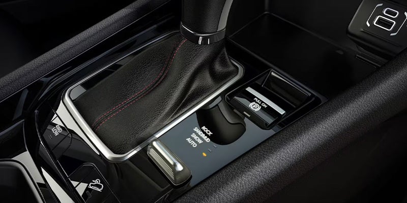 Close-up of a vehicle's gear shift console featuring a leather-wrapped gear shifter, control buttons, and a glossy black surface.