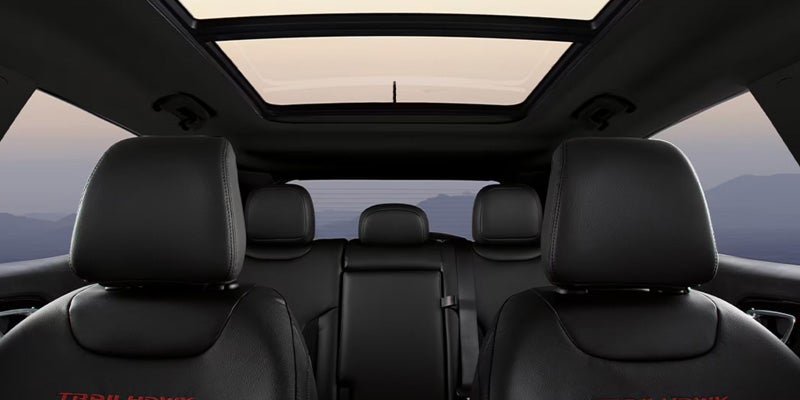 Interior view of a Jeep Compass showing black leather front and rear seats with a large panoramic sunroof and mountainous landscape visible outside.