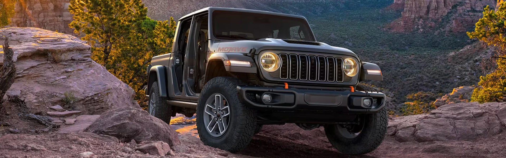 A black Jeep Gladiator parked on rocky terrain with mountains and trees in the background.