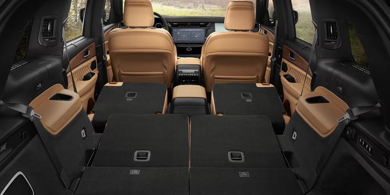Interior view of a spacious Jeep Grand Cherokee with tan leather seats, showcasing the back row and cargo area with seats folded down for extra storage space.