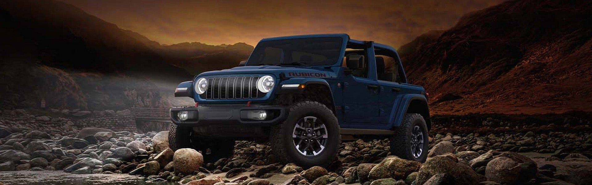 A blue Jeep Wrangler parked on rocky terrain with mountains in the background and a dramatic sky.