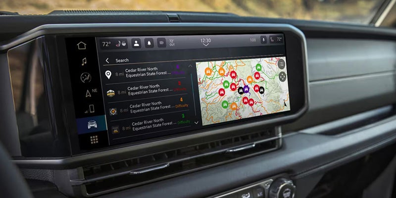 A close-up view of a Jeep Wrangler's touchscreen display showing a navigation map with various locations marked. The display is integrated into the dashboard, with climate control settings visible above.