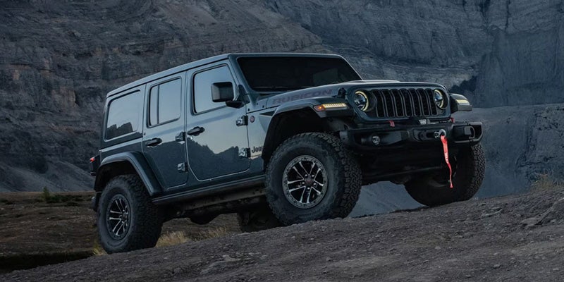 A black Jeep Wrangler parked on a rocky terrain with mountains in the background.