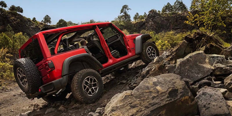 A red Jeep Wrangler navigating a rocky terrain with its doors removed.