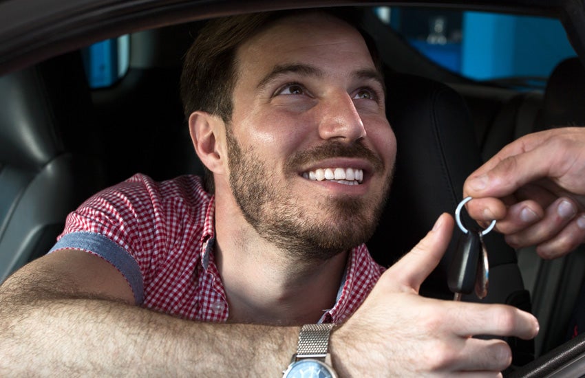 Man happily receiving car keys while sitting inside a new vehicle.