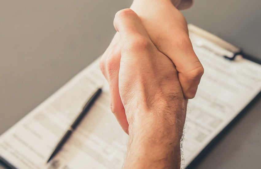 Two people shaking hands over signed documents with a pen nearby.