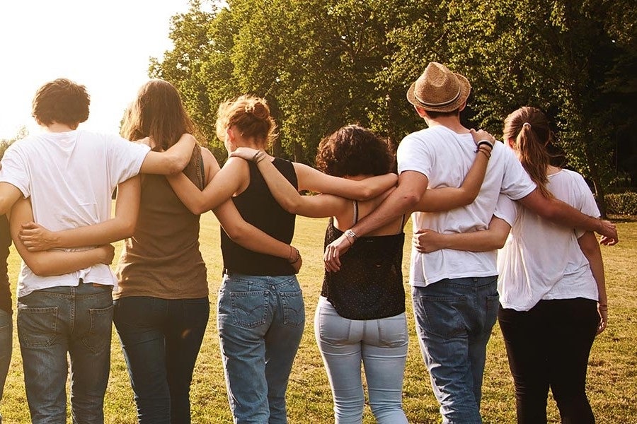 Group of friends standing arm-in-arm outdoors, enjoying a sunny day together.