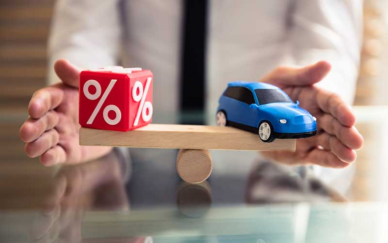 Balancing car purchase with interest rates symbolized by toy car and percentage cube on seesaw.