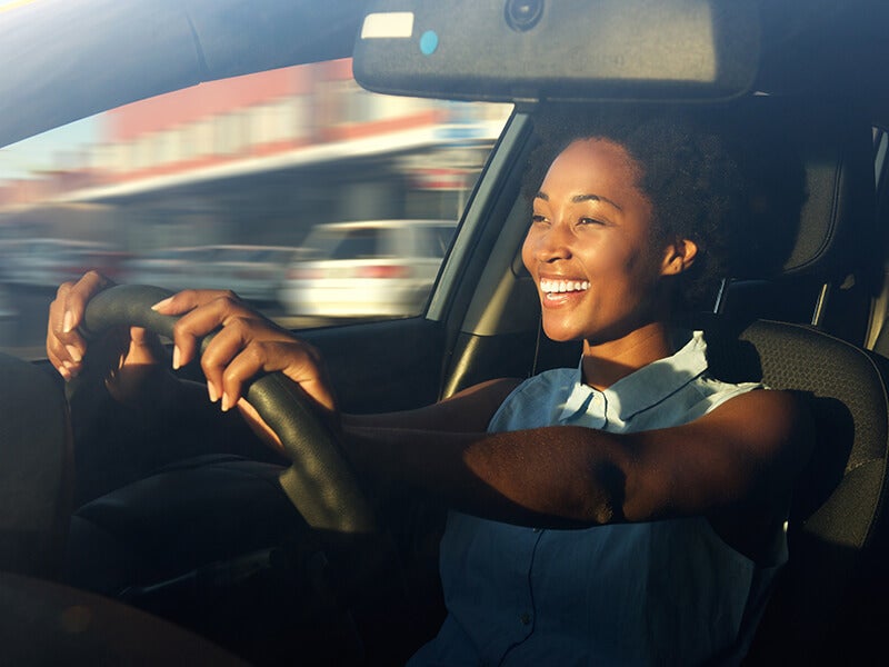 Smiling woman driving a car, enjoying a sunny day.