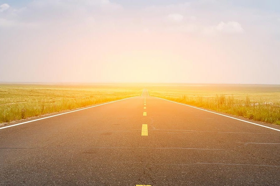 Empty highway stretching into horizon under a bright, glowing sky at sunrise or sunset.