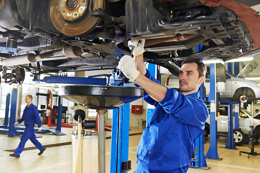 A mechanic working underneath a car on a lift in an auto repair shop.