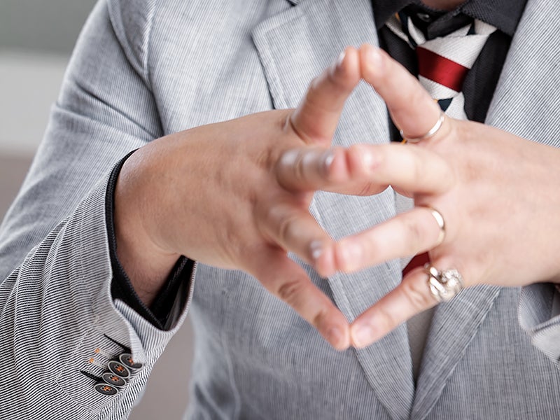 Person in suit making hand gesture, wearing rings and striped tie.